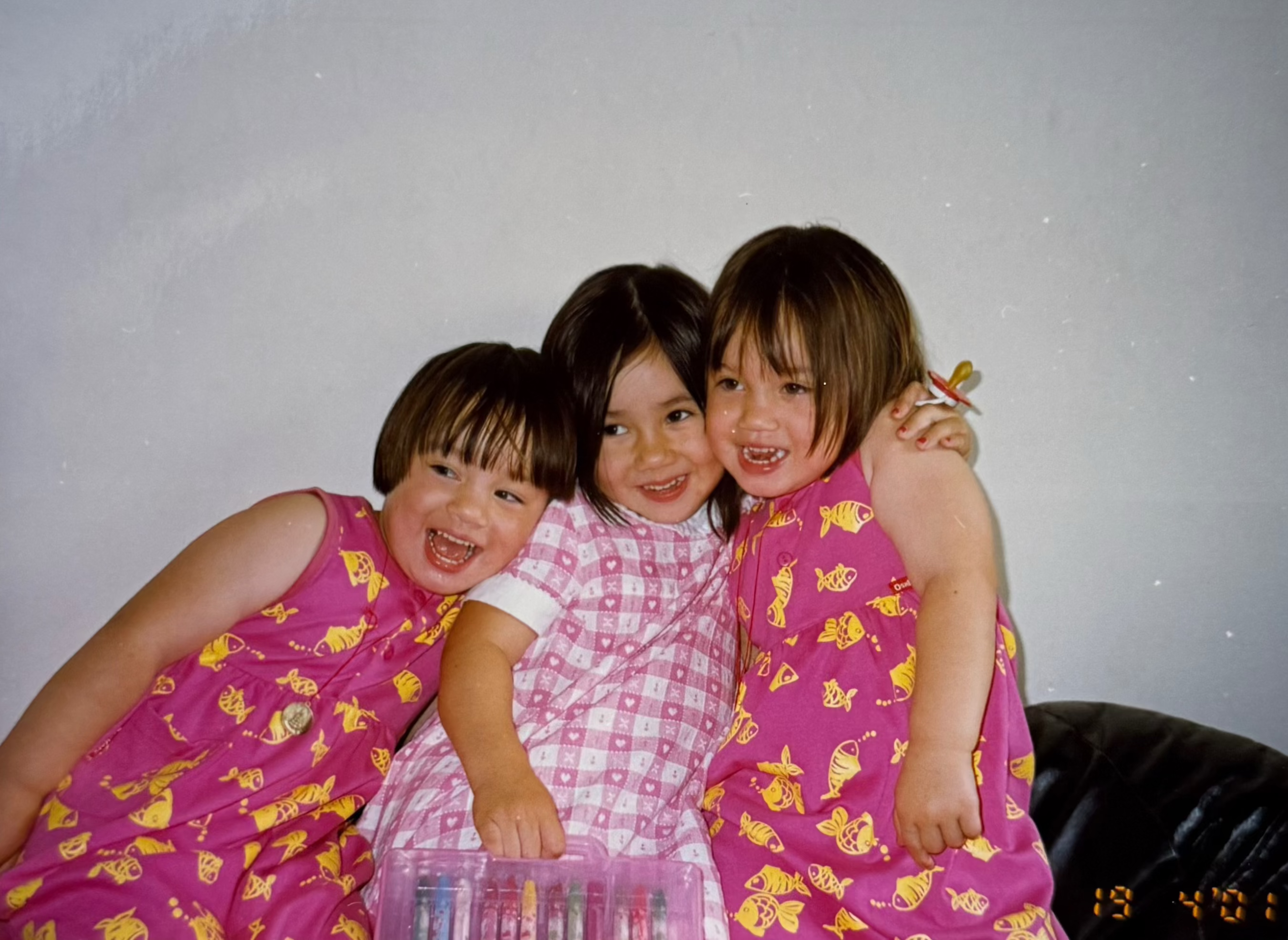 Three children in matching dresses posing together against a plain background